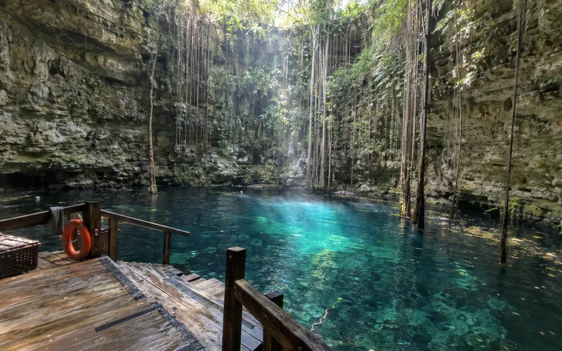 Clear blue-green cenote with hanging roots and a wooden swimming platform in Yucatan
