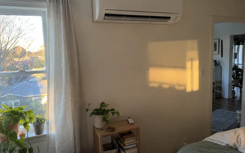 White mini-split air conditioner mounted high on a bedroom wall above a window