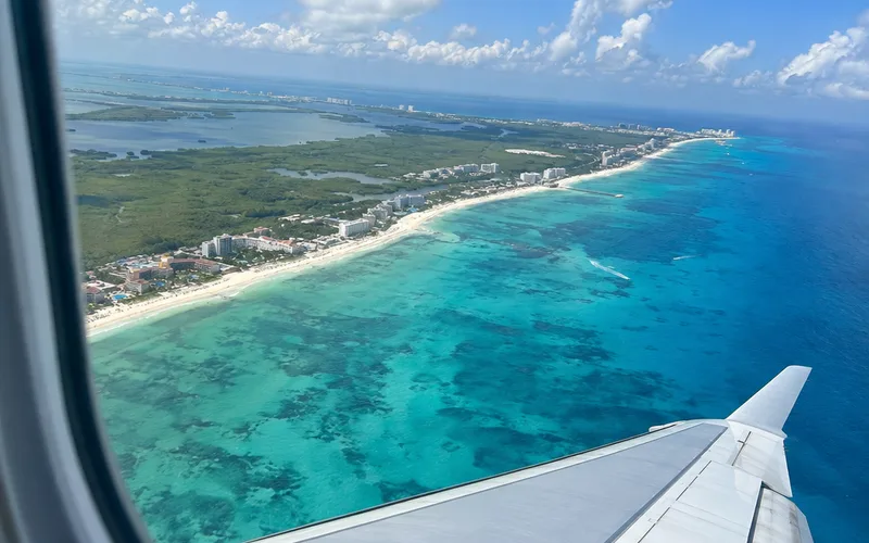 Airplane window view of turquoise water and the coastline near Cancun during descent