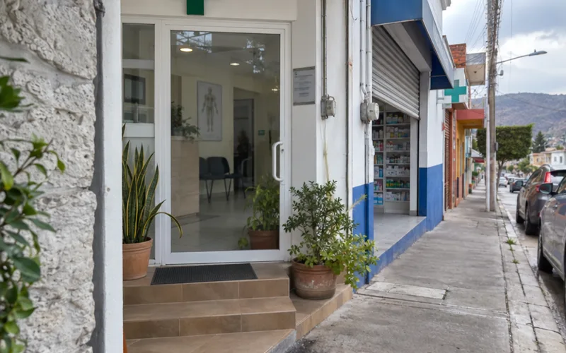 Entrance of a small private medical clinic with a green cross next to a pharmacy in Mexico