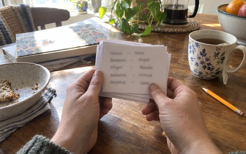 Hands holding a stack of handmade Spanish vocabulary flashcards at a kitchen table