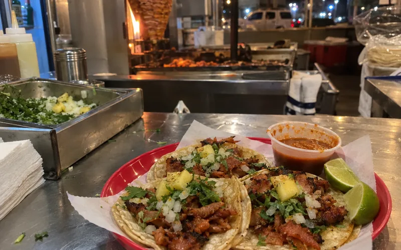Three street tacos with onion, cilantro and lime on a plate at an evening taco stand